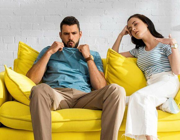 a couple on a couch dealing with uncomfortable heat that are in need of HVAC Service in Lansing, DeWitt, MI, Ingham County, Eaton County, Portland, MI